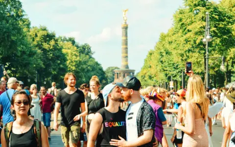 A couple kisses at a pride parade in Germany, with the Victory Column in the background. This scene shows Germany is gay friendly.