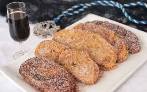 Torrijas cubiertas de azúcar y canela, listas para disfrutar. Un delicioso pan para torrijas, acompañado de una copa de vino dulce.