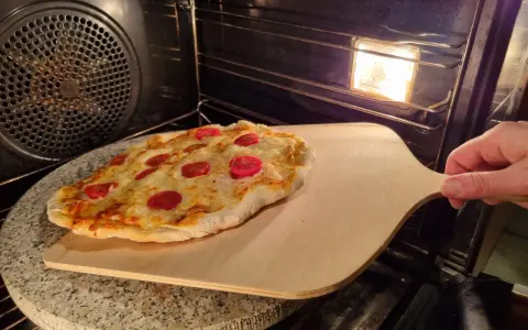 Pizza na kamieniu w piekarniku, gotowa do wyjęcia. Idealny sposób, jak piec pizzę na kamieniu dla chrupiącego spodu.