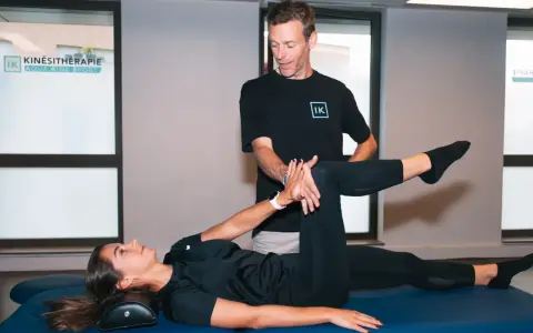 Un kinésithérapeute guide une patiente dans un exercice pour soulager la cruralgie. Elle est allongée sur une table de massage, une jambe pliée, l'autre tendue.