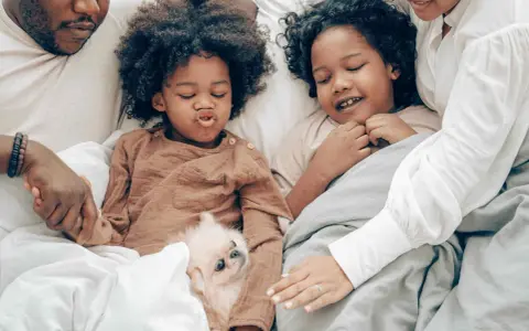Familie kuschelt im Bett, um sich mit Kindern zu entspannen. Ein kleiner Hund liegt zwischen ihnen.