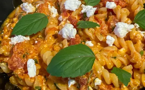 Makaron fusilli w pomarańczowym sosie z kawałkami sera i listkami bazylii.