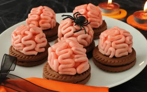 Gruselige Halloween-Nachspeise: Kekse mit Gehirn-förmiger rosa Glasur, dekoriert mit einer Spinne. Kerzen leuchten im Hintergrund.