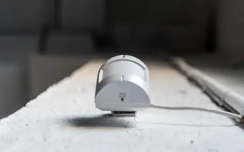 Detector de presencia y movimiento blanco, con cable, montado en superficie rugosa.
