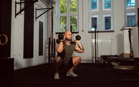 Mann macht Kniebeugen mit Kurzhanteln. Ein Supersatz ist, wenn zwei Übungen direkt hintereinander ohne Pause ausgeführt werden.