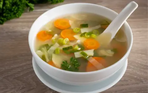 Tazón de sopa de verduras con zanahorias, puerros y perejil.