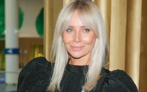 Blondynka z niebieskimi oczami i uroczą grzywką na boki, uśmiecha się lekko.