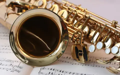 Ein glänzendes Musikinstrument, ein Saxophon, liegt auf Notenblättern. Seine goldene Oberfläche reflektiert das Licht.