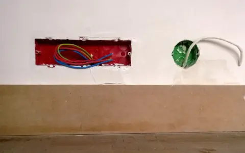 Boîtier rouge avec fils électriques colorés, prêt pour un interrupteur compteur électrique. Une boîte verte avec un câble blanc est visible à droite.