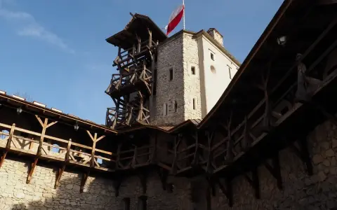 Zamek w Korzkwi z drewnianymi gankami i wieżą, na której powiewa polska flaga.