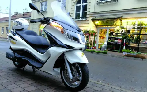 Biały skuter Piaggio X10 125, z kaskiem na siedzeniu, zaparkowany przed kwiaciarnią. Dane techniczne tego modelu są imponujące.