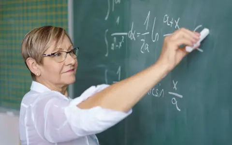 Nauczycielka matematyki pisze na tablicy wzory. Czy to zapowiedź podwyżki dla nauczycieli? Najnowsze wiadomości.