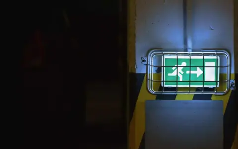 Panneau de sortie de secours vert lumineux, indiquant la direction à suivre. Le **baes signification** est claire : sécurité et évacuation.