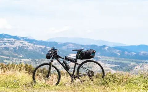 Rower gotowy do bike packingu, z sakwami na kierownicy i pod siodełkiem, na tle górskiego krajobrazu.