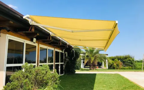 Tende da sole sconto in fattura, gialle e moderne, proteggono un edificio con ampie vetrate da un sole splendente.