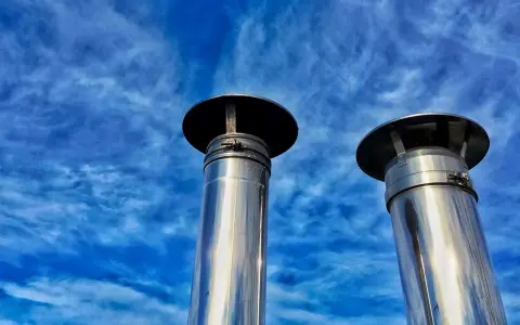 Due camini in acciaio inox, modello uni 7129 scarico a parete, brillano sotto un cielo blu con nuvole sottili.