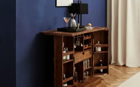 Elegante mobile bar design in legno scuro, aperto, con bottiglie, bicchieri, lampada e decorazioni.