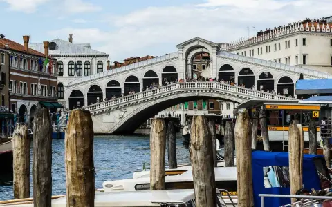 Le célèbre pont du Rialto à Venise, animé par des touristes, surplombe le Grand Canal où naviguent des gondoles et des taxis nautiques.