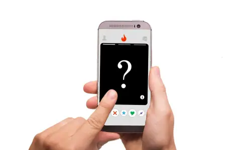 Dłoń trzyma smartfon z aplikacją randkową. Na ekranie widnieje znak zapytania i ikony: X, gwiazdka, serce, błyskawica. To **Tinder oznaczenia** – decyzja należy do Ciebie!