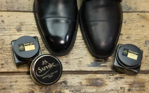 Czarne, eleganckie buty i dwa słoiczki Saphir: krem do skóry i olejek. Idealne, by dowiedzieć się, czym natłuścić skórzane buty.