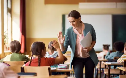Uśmiechnięta nauczycielka daje piątkę uczennicy. To pozytywna ocena pracy nauczyciela początkującego, który buduje relacje z uczniami.