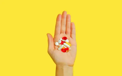 Hand hält bunte Pillen und Kapseln, die bei der Behandlung von Akne helfen könnten, wie z.B. Vitamin B5.