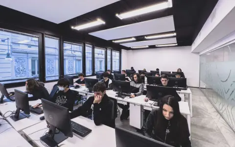 Giovani studenti concentrati davanti ai computer, un'aula moderna che ospita un corso di programmazione gratis.