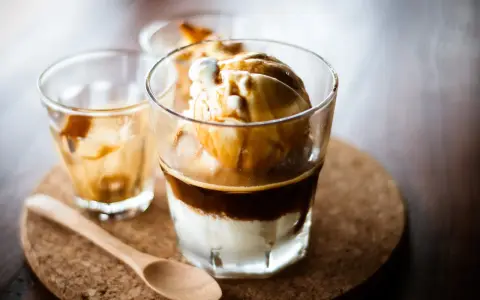 Ein italienischer Eiskaffee, Affogato, mit Vanilleeis und heißem Espresso. Ein Holzlöffel liegt daneben.