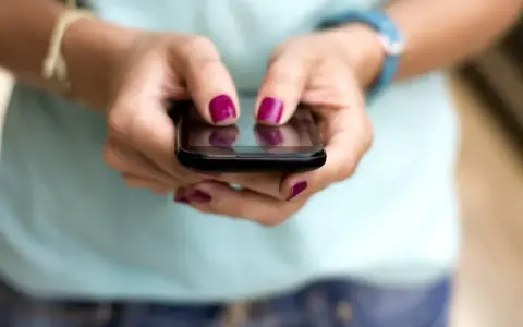 Dłonie z malowanymi paznokciami piszą na telefonie, być może ustawiając ipko zmiana limitu przelewu.