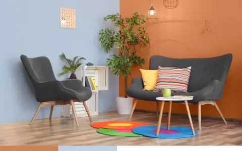 Nowoczesny salon z szarymi fotelami i kanapą, akcentem jest ściana w kolorze oranżowym.