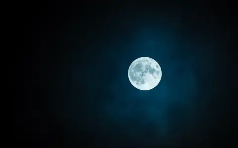 Jasny księżyc w pannie, otoczony mglistą poświatą, góruje na ciemnym, nocnym niebie.