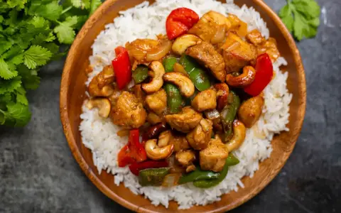 Un délicieux poulet noix de cajou servi sur un lit de riz blanc. Des poivrons rouges et verts ajoutent de la couleur à ce plat savoureux.