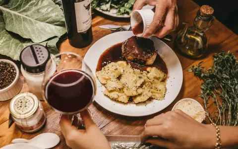 Elegancka kolacja z ravioli i wołowiną w sosie. Idealne pytanie: jakie wino do gotowania? Czerwone wino i świeże zioła dopełniają atmosferę.