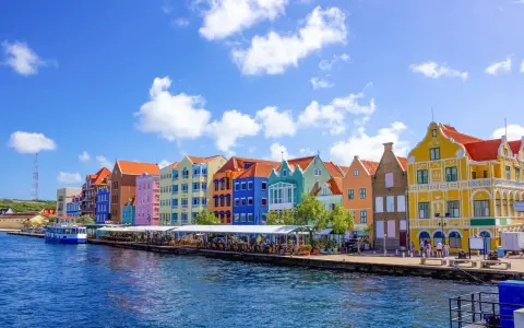 Färgstarka hus längs en kaj, en båt i vattnet. Här kan man se var ligger Curacao, en karibisk pärla.