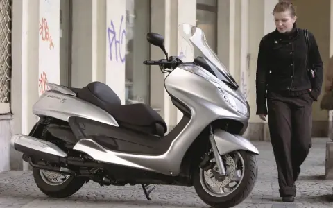 Srebrny skuter Yamaha Majesty 400, symbol miejskiej elegancji, obok kobiety w ciemnej kurtce.