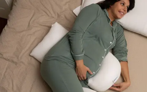 Donna incinta, con pigiama verde, si rilassa a letto con un cuscino di supporto, alleviando la stanchezza in gravidanza.