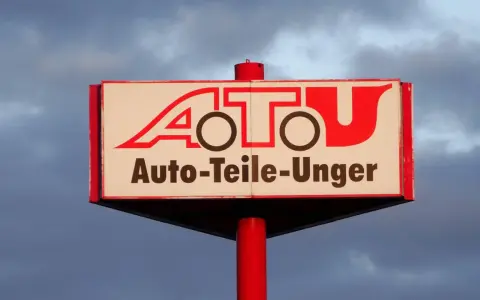 Schild mit rotem Schriftzug "A.T.U. Auto-Teile-Unger" vor bewölktem Himmel.