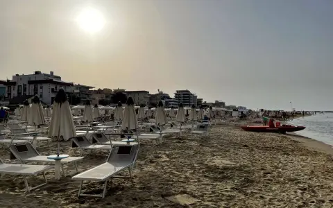 Spiaggia di Igea Marina con lettini e ombrelloni chiusi, bagnino pronto con la sua imbarcazione sul mare calmo.
