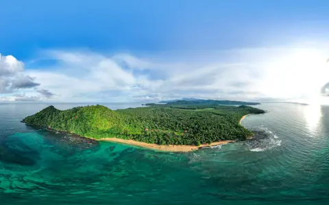 Zielona wyspa z palmami i plażą, otoczona turkusową wodą. Widok na Sao Tome z lotu ptaka.