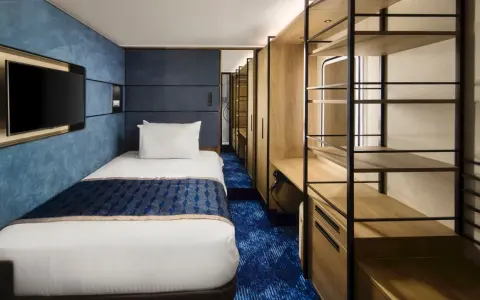 Interno cabina singola nave da crociera: letto, TV a parete, armadio aperto con mensole e scrivania. Le dimensioni delle cabine sono ottimizzate per il comfort.