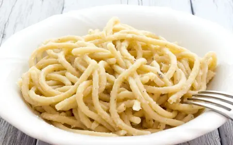 Pici, pasta fatta a mano con un'origine antica, servita in una ciotola bianca con una forchetta.