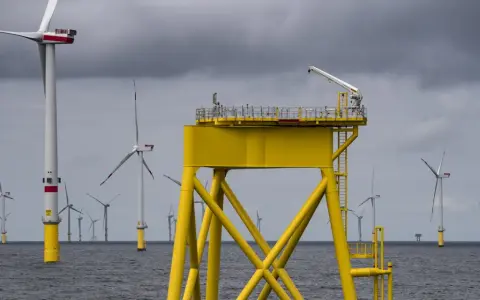 Große gelbe Plattform mit Kran inmitten vieler Windkraftanlagen im Meer. Die Zukunft der Windkraft onshore und offshore.