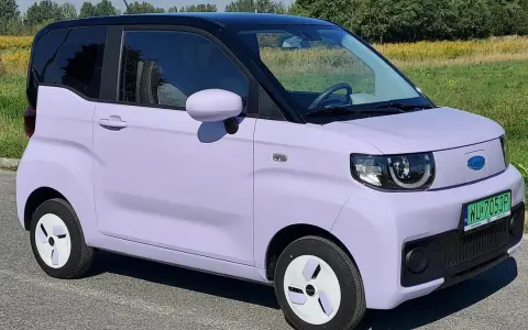 Jasnofioletowy, elektryczny **Exlantix** z czarnym dachem, zaparkowany na tle zieleni.