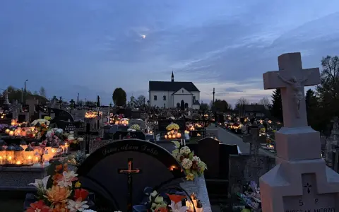 Cmentarz nocą, pełen płonących zniczy i kwiatów. W oddali kościół, a na niebie księżyc. Modlitwa świętej Gertrudy w ciszy zadumy.