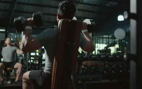 Två män tränar axlar med hantlar på ett gym. En fokuserar på push, den andra på pull.