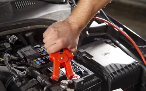 Starthilfe: Rote Klemme am Pluspol, warum nicht minus an minus? Ein Mann klemmt ein Starthilfekabel an die Autobatterie.