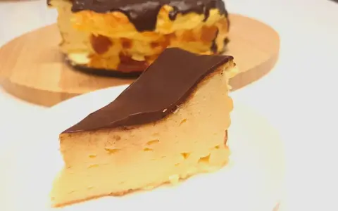 Kawałek puszystego keto sernika z mascarpone, polany czekoladą. Cały sernik w tle.