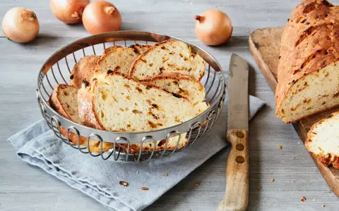 Frisch gebackenes Zwiebelbrot, bereit für ein leckeres Zwiebelbrot Rezept. Ganze Zwiebeln liegen daneben.