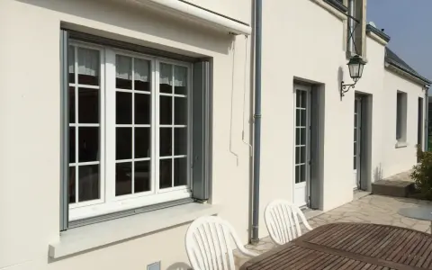 Un grand **appui de fenêtre** blanc orne la façade d'une maison. Des volets gris sont partiellement ouverts.