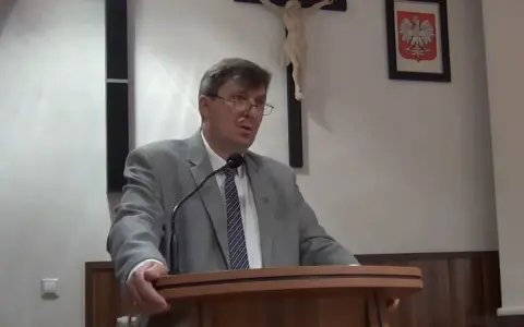 Mężczyzna w garniturze przemawia, za nim krzyż i godło Polski. Może mówi o cnotach kardynalnych.